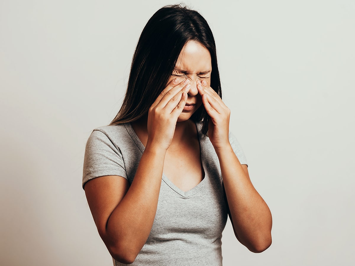 A woman with sinus pressure puts her hands on her nose