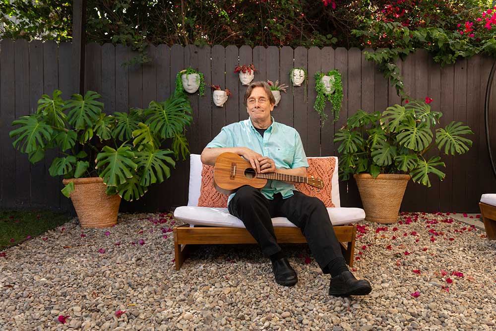 USC Norris Comprehensive Cancer Center patient Mike Snow, seated outdoors, playing the ukulele.