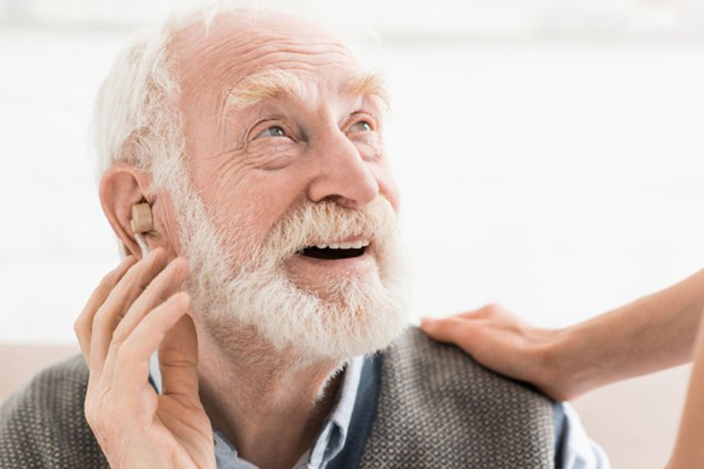 A man looking happy wearing a hearing aid.